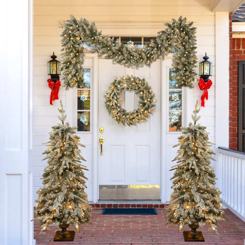 Decorative Christmas setup with wreaths, trees, and lights on a front door.
