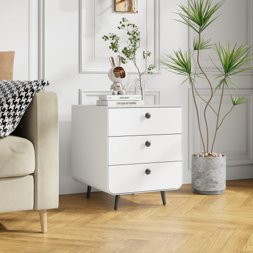 White dresser with three drawers in a room with a chair, plant, and decorative items.